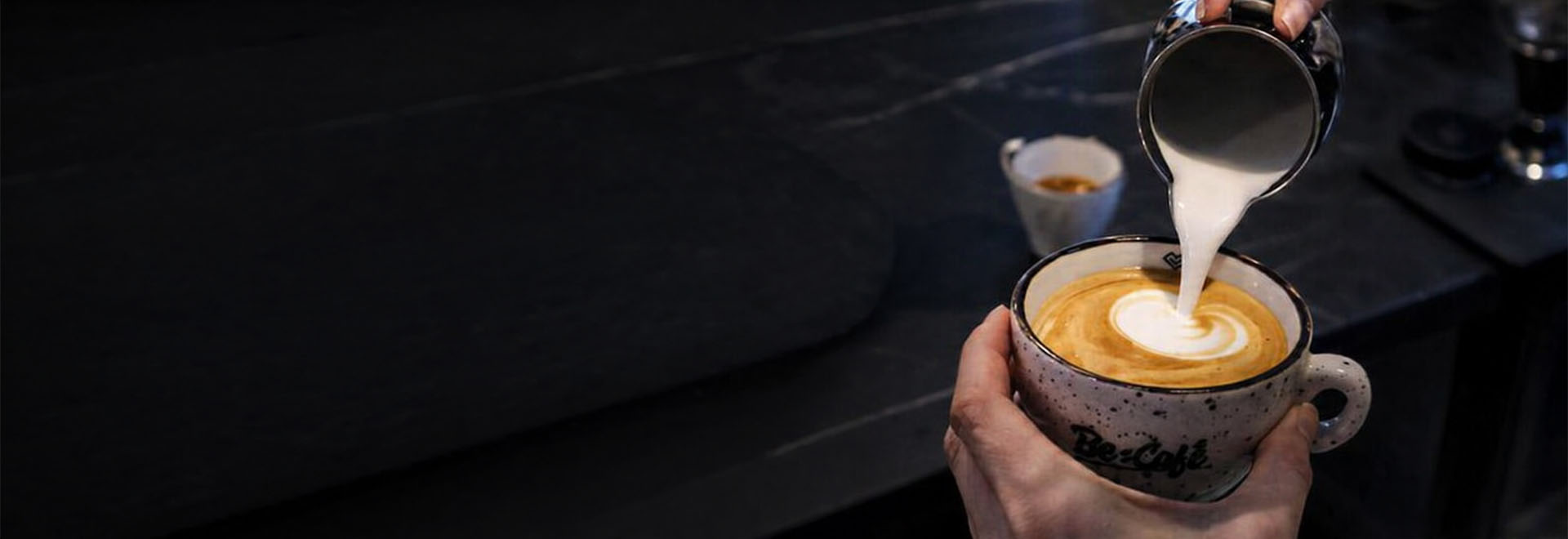 Barista nalieva napenené mlieko do kávy a vytvára latte art v šálke Be:Café